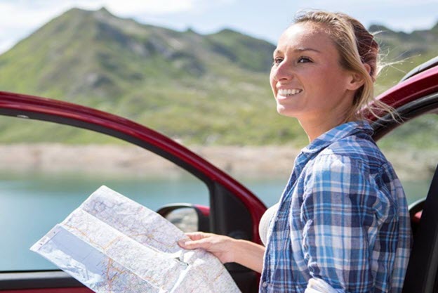 Woman holding map outside red car