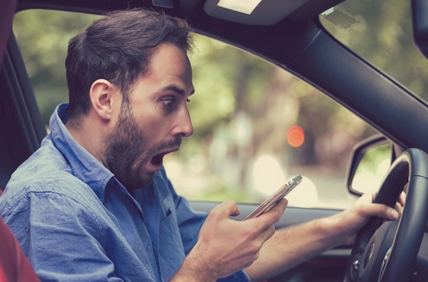 Man sitting inside the car with mobile phone in hand texting while driving