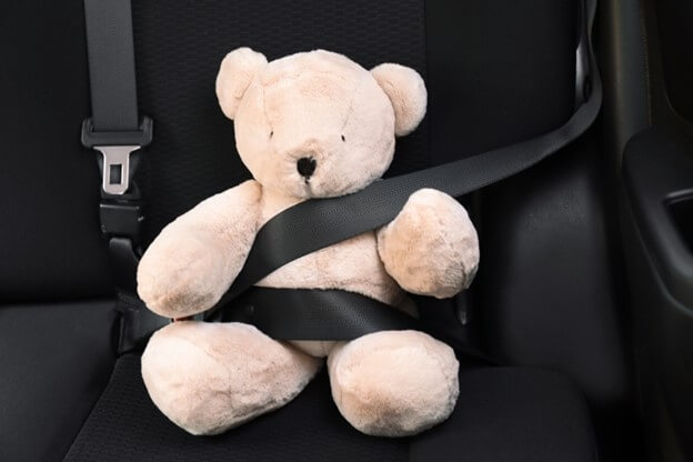 Toy bear buckled with a safety belt on in the backseat.